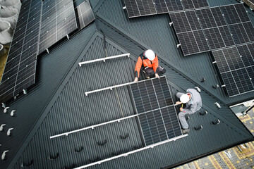 Mounters building photovoltaic solar module station on roof of house. Men electricians in helmets...