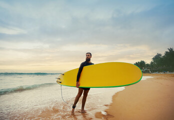 Young  bearded man with surfboard standing near a beach. Man with surfing board outdoors on a...