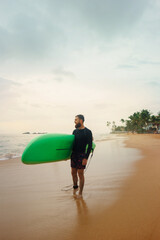 Young  bearded man with surfboard standing near a beach. Man with surfing board outdoors on a summer day.