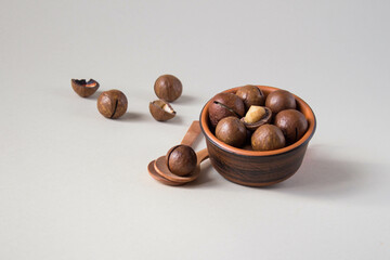 Macadamia nuts in ceramic bowl on beige background. Nuts with sawn nutshells and with opener key on the wooden spoon. Healthy snack, superfood.