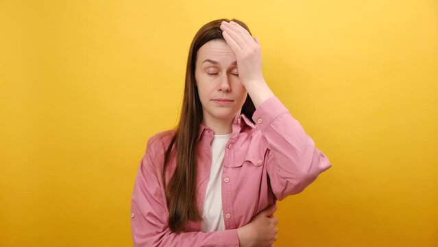 Portrait of unlucky sad young woman making facepalm gesture, feeling regret and sorrow, blaming herself for mistake, frustrated by defeat, posing isolated over yellow color background wall in studio