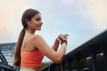 Portrait of beautiful sporty woman  in sportswear using smartwatch and wireless earbud while resting