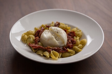 Pesto conchiglie with sundried tomatoes and burrata cheese served in white plate
