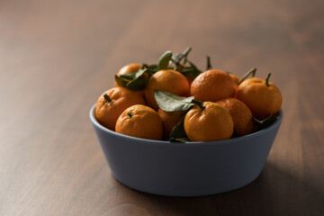 Small organic tangerines with leaves in ceramic bowl on wood table