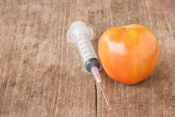 Fresh tomato and syringe on wooden table