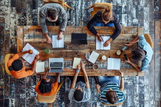 Above view of group of multi ethnic business people working in an office. Team of business people working on project in office, using laptop, writing notes at table with books, learning, Generative AI