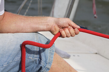 Red boat rope in the hand . Man skipper controls a yacht in the port