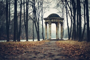 The old rotunda in the park in autumn. Silhouettes of naked black trees without leaves during the fall season. Melancholic landscape