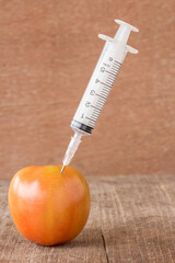 Fresh tomato and syringe on wooden table