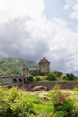 Fototapeta na wymiar Clouds gather over the historic Eilean Donan Castle, where a stone bridge connects the iconic Scottish landmark to lush greenery, with the fluttering flag