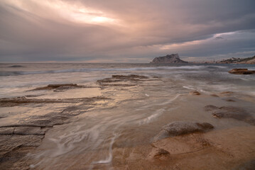 Fototapeta na wymiar Coastal landscape with the Peñon de Ifach on the horizon. The sea is calm and the sky is cloudy.
