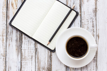Coffee cup and notebook on white wooden table