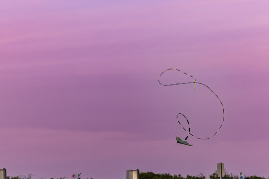 Kite flying through pink and purple sunset sky with long swirling tail
