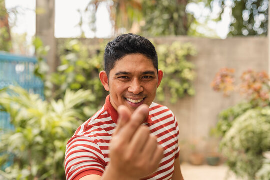 Smiling Asian man making a heart sign with his fingers in an outdoor setting
