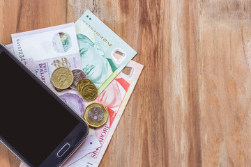 Smart phone and singapore dollar on wooden table