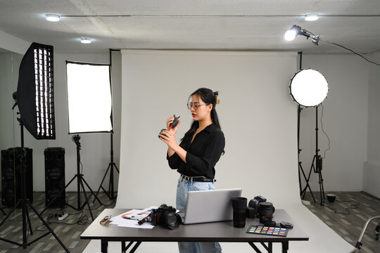 Female photographer cleaning camera lens with rubber air blower at her studio