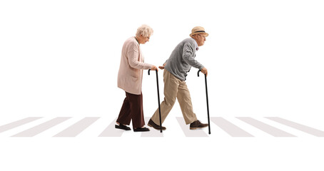 Full length profile shot of an elderly man and an elderly woman with canes walking at a pedestrian...