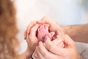 Small feet of newborn baby in parents hands. Copy space. White background. Mom and dad Love and...