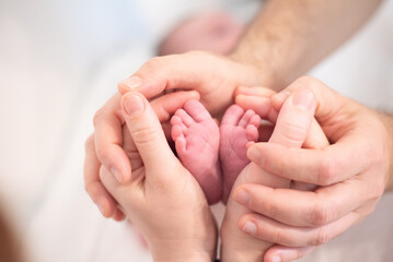 Small feet of newborn baby in parents hands. Copy space. White background. Mom and dad Love and care baby.