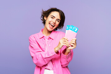 Smiling, attractive woman in pink, with brunette hair, holding travel tickets and documents