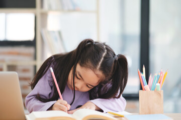 A young girl is sitting at a desk with a pencil and a book