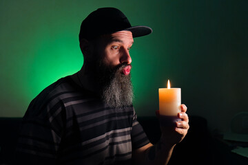 Bearded man holding a lit candle in his hand. Green background