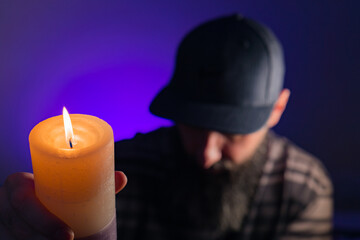 Bearded man holding a lit candle in his hand. Purple background