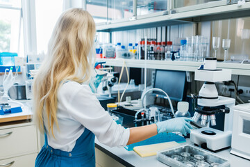 blonde long-haired woman in overalls servicing laboratory equipment located on a table.Science lab concept.