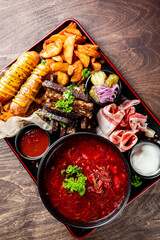 A vibrant display of a hearty meal featuring grilled meat, assorted fried sides, fresh vegetables, and a bowl of red soup, showcasing a mix of textures and colors.