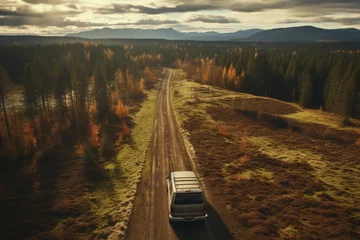 Fototapeten Beautiful aerial view of old red vintage car driving along stunning autumn forest road at sunset © Nikolai