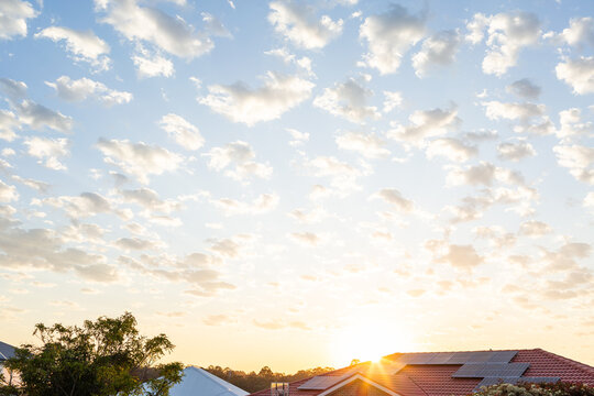 Clouds dotting the sunrise sky above houses with solar on the roof