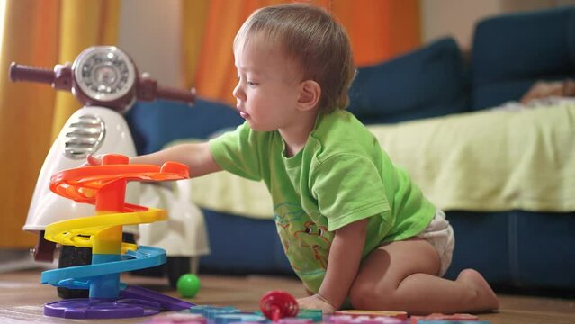 baby child plays with a toy slide and rolls a ball. happy family kid dream concept. baby play indoors with toys develops fine lifestyle motor skills. baby plays with toys in kindergarten