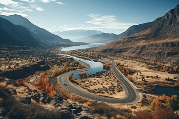 Aerial view of winding paved serpentine road next to river in scenic autumn mountains - obrazy, fototapety, plakaty