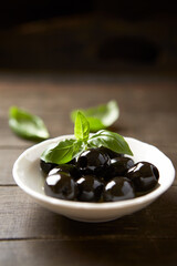 Black olives with fresh basil on rustic wooden background. Soft focus. Close up.	