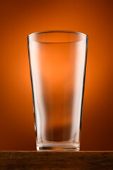 an one empty glass on a wooden stand and a light brown background, object close view