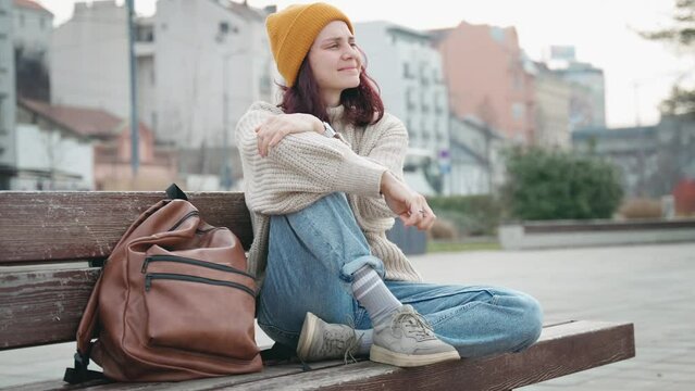 A young Caucasian woman is sitting on a bench in the city and enjoying the fresh air