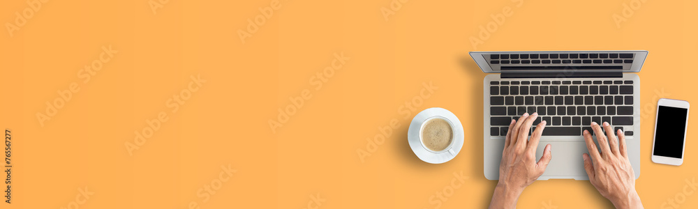 Wall mural person hand using laptop computer from above with coffee and smartphone on orange background.