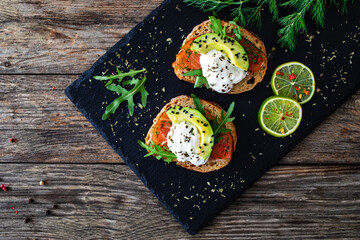 Tasty sandwiches - toasted bread with burrata cheese, smoked salmon, avocado and arugula on wooden...