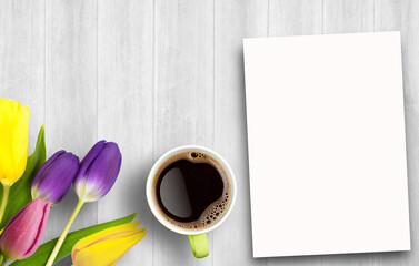 Colorful tulips bouquet and blank greeting card and coffee on white wooden table background.