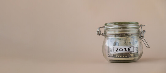 Saving Money In Glass Jar filled with Dollars banknotes. 2025 year transcription in front of jar....