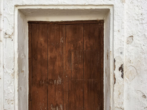 Puerta de madera rústica en una pared encalada en Sanlúcar de Guadiana, España. Puerta cerrada y pintada de marrón de una casa antigua y deshabitada.