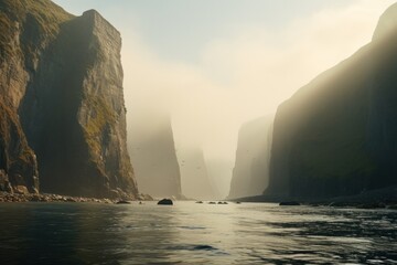 The tranquil and misty landscape consists of towering cliffs. The calm sea and soft sunlight shine through the haze. - obrazy, fototapety, plakaty