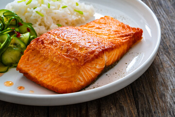 Seared salmon steak with boiled white rice and sliced cucumber on wooden table
- 765586653