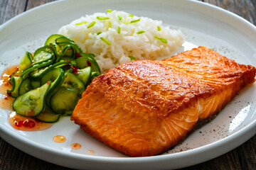 Seared salmon steak with boiled white rice and sliced cucumber on wooden table
- 765586821