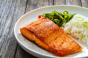 Seared salmon steak with boiled white rice and sliced cucumber on wooden table
- 765586862