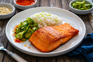 Seared salmon steak with boiled white rice and sliced cucumber on wooden table
- 765587033