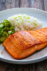 Seared salmon steak with boiled white rice and sliced cucumber on wooden table
- 765587067