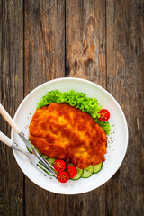 Crispy breaded fried pork chop and fresh vegetables on wooden table
