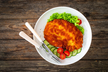 Crispy breaded fried pork chop and fresh vegetables on wooden table
- 765588690