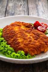 Crispy breaded fried pork chop and fresh vegetables on wooden table
- 765589651
